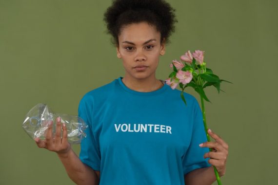 Portrait of a volunteer promoting environmental conservation, holding recycled plastic and flowers.